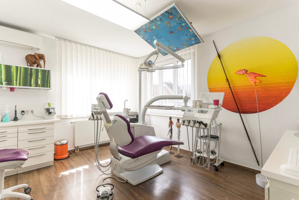 Helle Zahnarztpraxis mit Behandlungsstuhl und Wanddekoration.