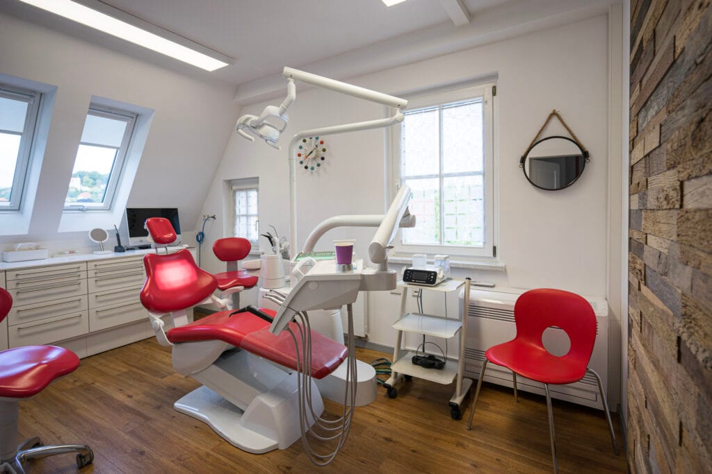 Moderne Zahnarztpraxis mit roten Stühlen.