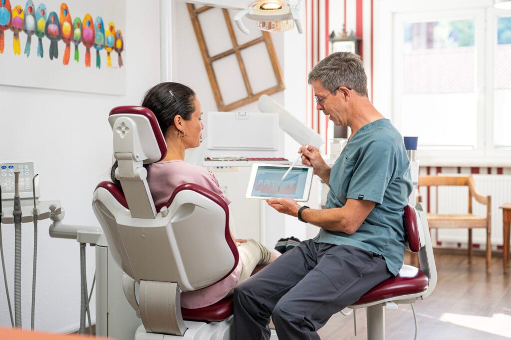 Zahnarzt Frank Naumann erklärt Patientin Zahnbehandlung am Tablet.